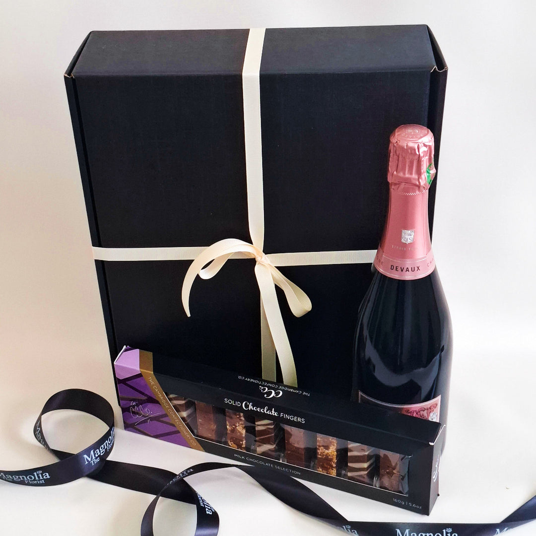 Bottle of rose champagne and chocolate truffles in a black gift box with a white ribbon.