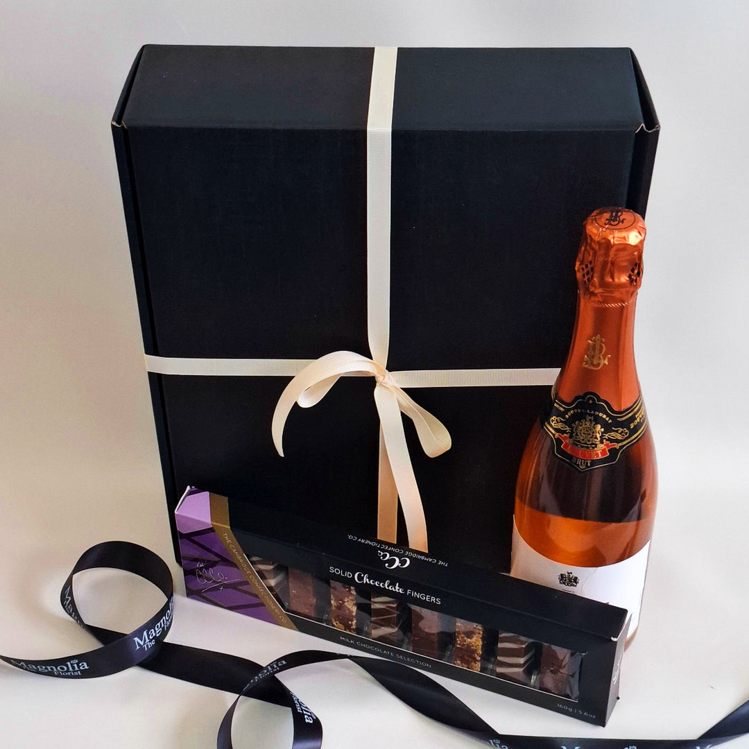 Bottle of sparkling rose wine and chocolate truffles in a gift box with a black ribbon.