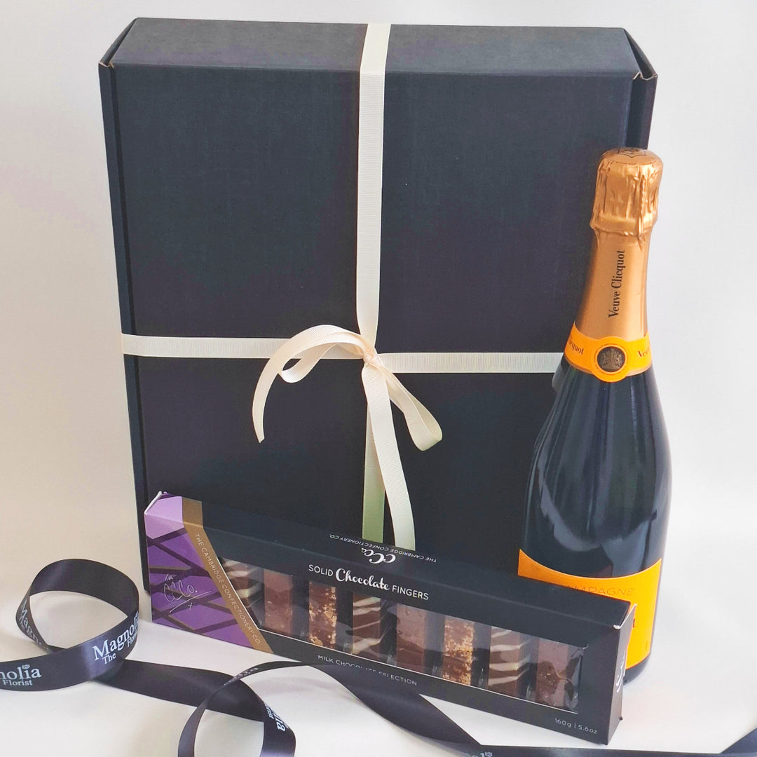 Bottle of premier champagne and chocolate fingers in front of a wrapped gift box.