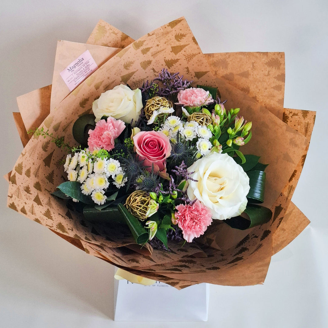 Bouquet of pink and white toned flowers wrapped in kraft paper with a 'MAGNOLIA' branded white bag underneath.