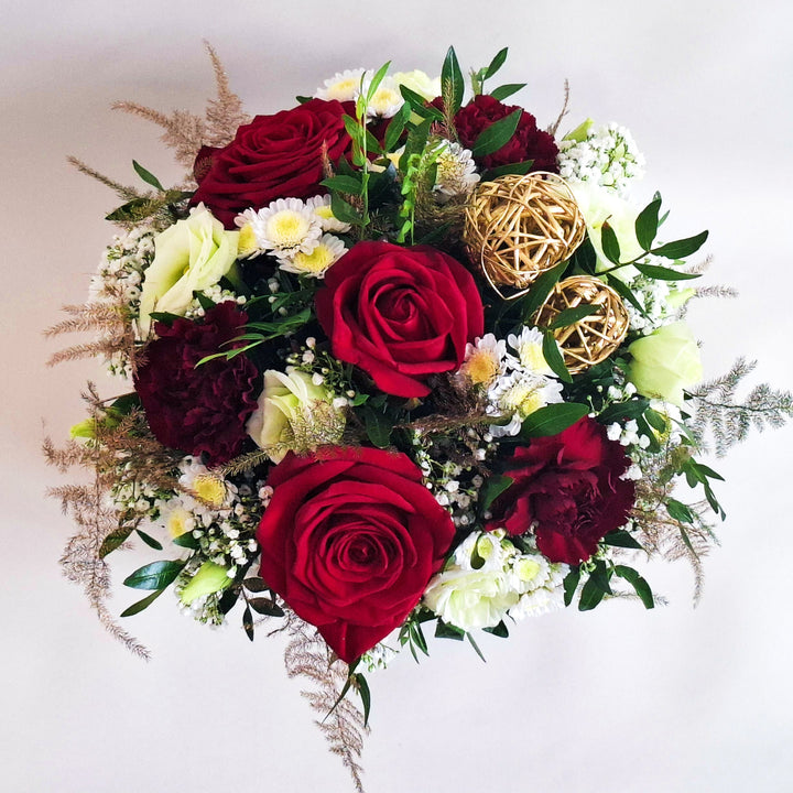 Floral arrangement with red and burgundy roses, greenery, and decorative elements in a black box.