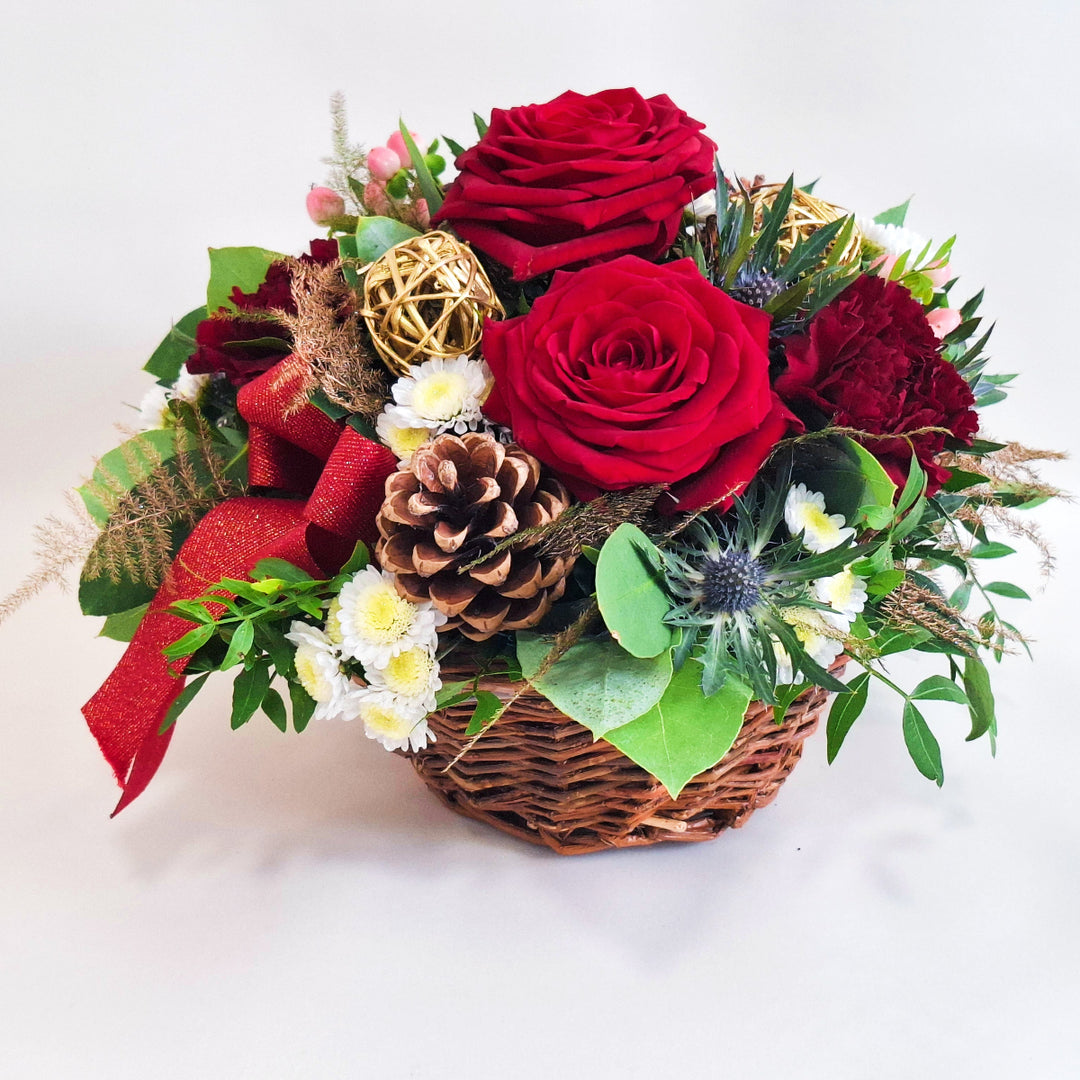 Arrangement of red roses, pinecones, and greenery in a wicker basket