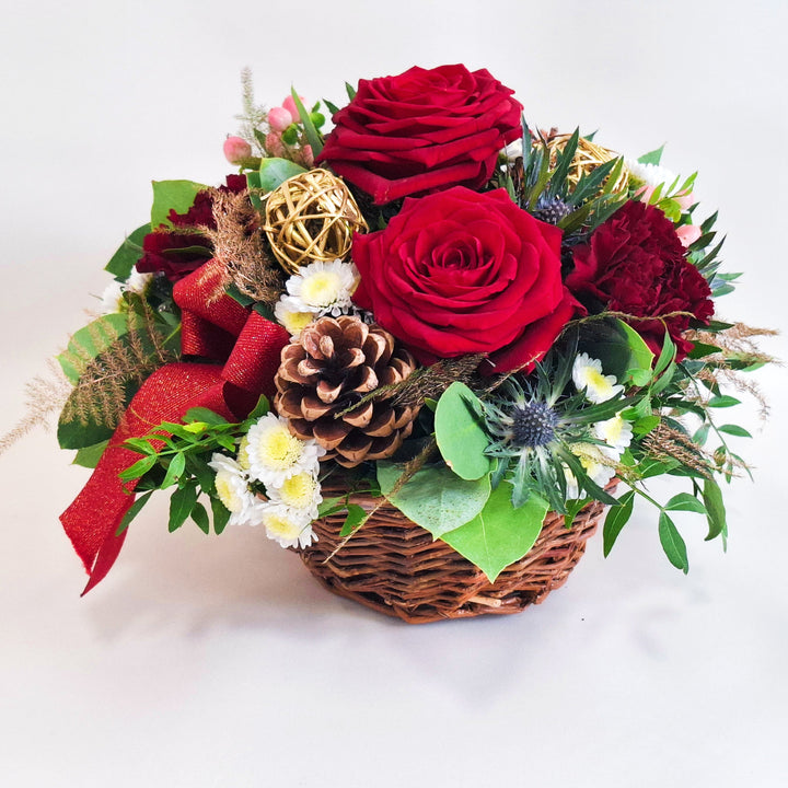 Arrangement of red roses, pinecones, and greenery in a wicker basket