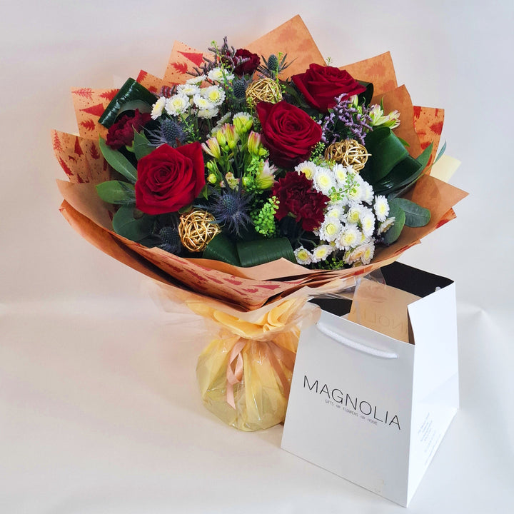 A bouquet of flowers, in red, white and pink tones, wrapped in kraft paper and in oue Magnolia branded gift bags.