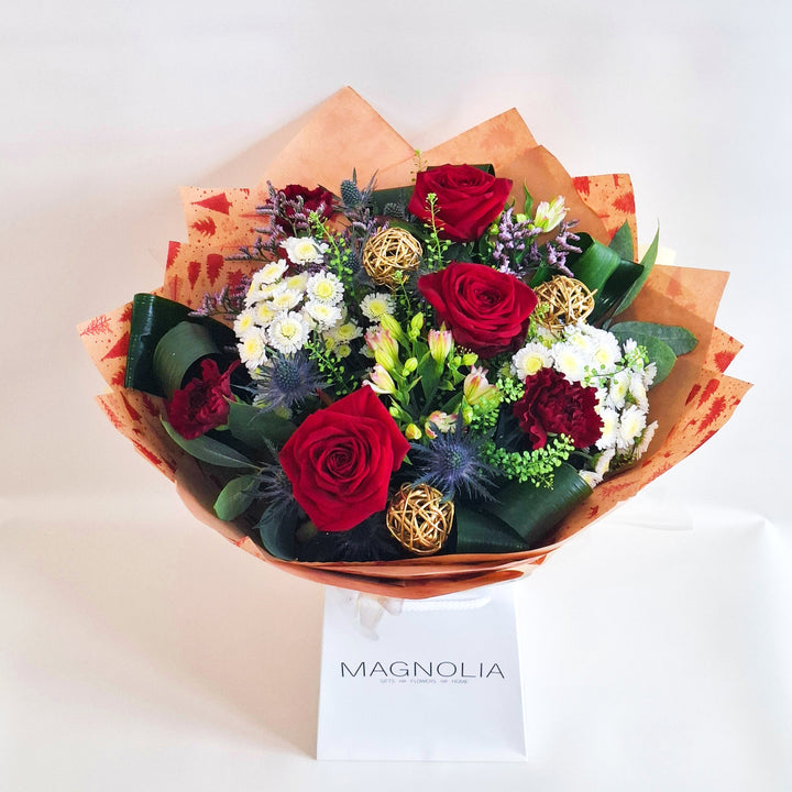 A bouquet of flowers, in red, white and pink tones, wrapped in kraft paper and in oue Magnolia branded gift bags.