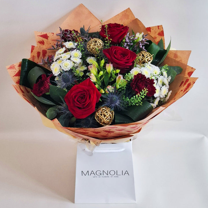A bouquet of flowers, in red, white and pink tones, wrapped in kraft paper and in oue Magnolia branded gift bags.