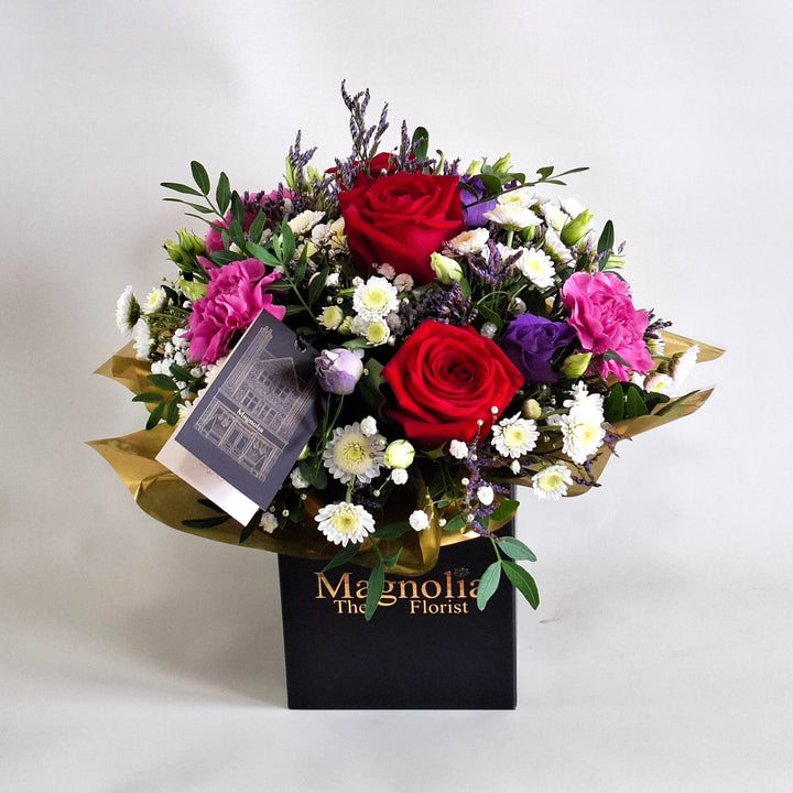 Dainty Belvedere Arrangement - Magnolia the Florist Belvedere blends rich red roses with cerise carnations, white chrysanthemum, purple lisianthus, limonium, gyp and pistache to create a romantic, luxurious floral arrangement. Presented in our Magnolia‑branded box and arranged in floral foam for long‑lasting freshness. For scale purposes, our branded box is 15cm(h) x 12cm(w) x 12cm(d), giving an overall size of approximately 25cm(h) x 18cm(w).  1