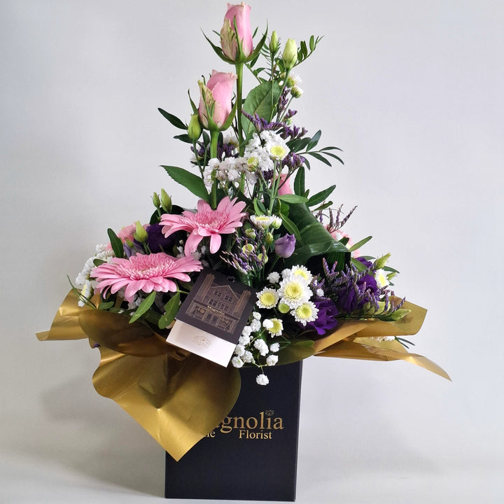 Islay Arrangement - Magnolia the Florist Islay is a soft, feminine floral arrangement crafted with pink roses, pink carnations, pink germini, white chrysanthemum, purple lisianthus, folded aspidistra, limonium, gyp and pistache. Presented in our Magnolia‑branded box and arranged in floral foam for long‑lasting freshness. For scale purposes, our branded box is 15cm (h) x 12cm (w) x 12cm (d), giving an overall size of approximately 35cm (h) x 18cm (w).  1