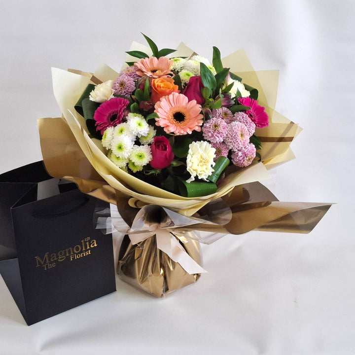 Joy For Mum Hand-tied Bouquet - Magnolia the Florist Celebrate Mother's Day with this stunning hand-tied bouquet crafted especially for mum. A blend of roses, germini, carnations, and chrysanthemums in cerise, peach, pink, and white tones creates a joyful arrangement that radiates warmth and appreciation. Presented in our signature Magnolia branded box bag, this bouquet arrives fresh and ready to brighten her day with elegance and charm.  1