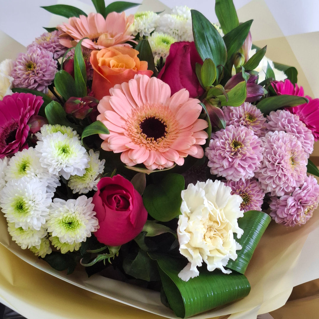 Joy For Mum Hand-tied Bouquet - Magnolia the Florist Celebrate Mother's Day with this stunning hand-tied bouquet crafted especially for mum. A blend of roses, germini, carnations, and chrysanthemums in cerise, peach, pink, and white tones creates a joyful arrangement that radiates warmth and appreciation. Presented in our signature Magnolia branded box bag, this bouquet arrives fresh and ready to brighten her day with elegance and charm.  2