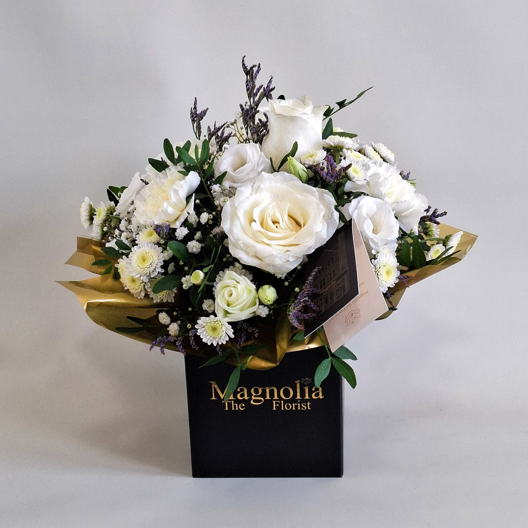 Dainty Kew Arrangement - Magnolia the Florist Kew is a serene all‑white floral arrangement inspired by botanical elegance. Featuring white roses, white carnations, white chrysanthemum, white lisianthus, limonium, gyp and pistache. Presented in our Magnolia‑branded box and arranged in floral foam for long‑lasting freshness. For scale purposes, our branded box is 15cm (h) x 12cm (w) x 12cm (d), giving an overall size of approximately 25cm (h) x 18cm (w).  1