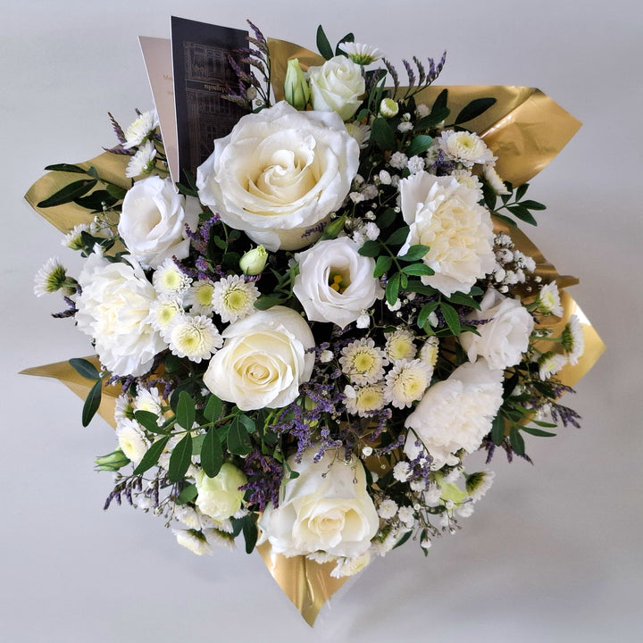 Dainty Kew Arrangement - Magnolia the Florist Kew is a serene all‑white floral arrangement inspired by botanical elegance. Featuring white roses, white carnations, white chrysanthemum, white lisianthus, limonium, gyp and pistache. Presented in our Magnolia‑branded box and arranged in floral foam for long‑lasting freshness. For scale purposes, our branded box is 15cm (h) x 12cm (w) x 12cm (d), giving an overall size of approximately 25cm (h) x 18cm (w).  2
