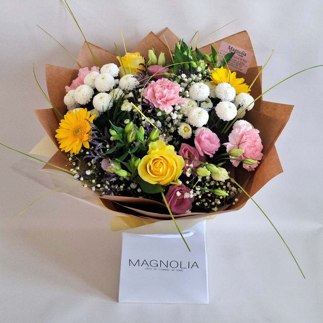 Bouquet of flowers wrapped in brown paper, in shade sof pink, white and yellow and in a Magnolia the Florist Branded Bag.
