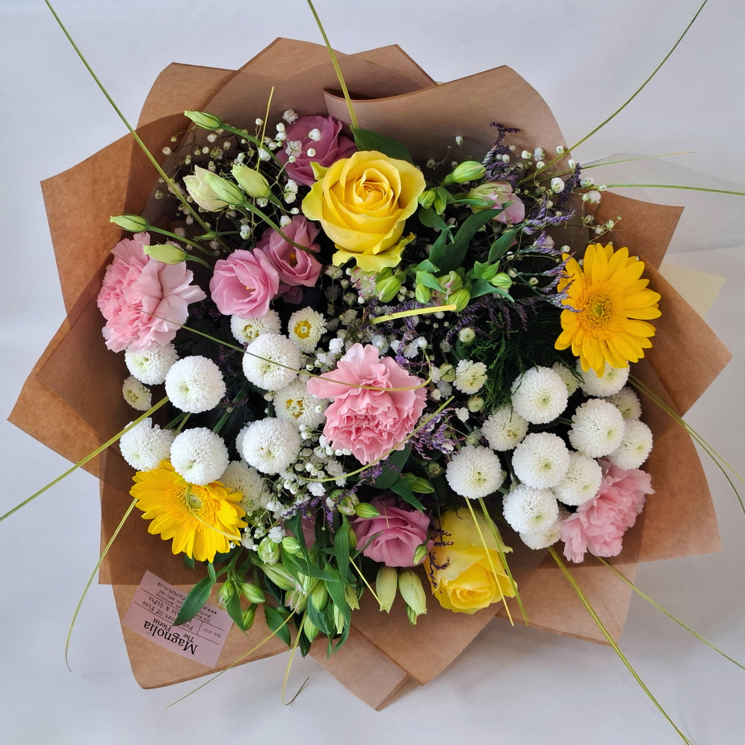 Bouquet of flowers wrapped in brown paper, in shade sof pink, white and yellow and in a Magnolia the Florist Branded Bag.