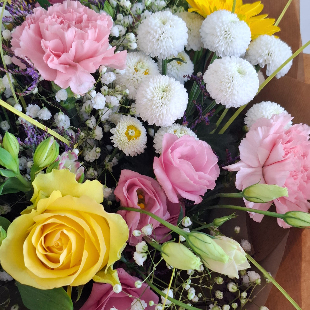 Bouquet of flowers wrapped in brown paper, in shade sof pink, white and yellow and in a Magnolia the Florist Branded Bag.