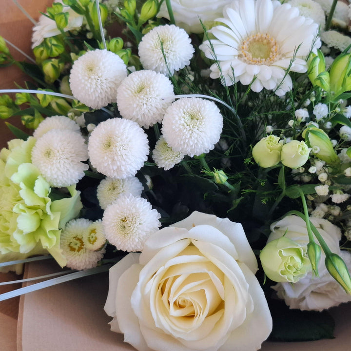 Bouquet of flowers wrapped in brown paper, in shades of white and Green and is presented a Magnolia the Florist Branded Bag.
