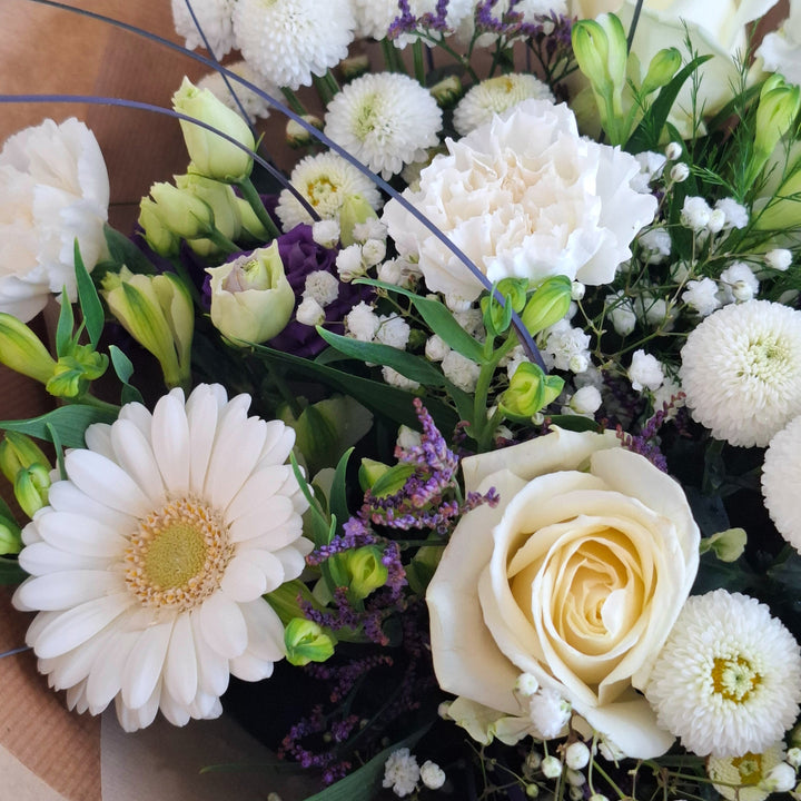 Bouquet of white and purple flowers wrapped in brown paper, presented in a Magnolia the Florist branded bag.