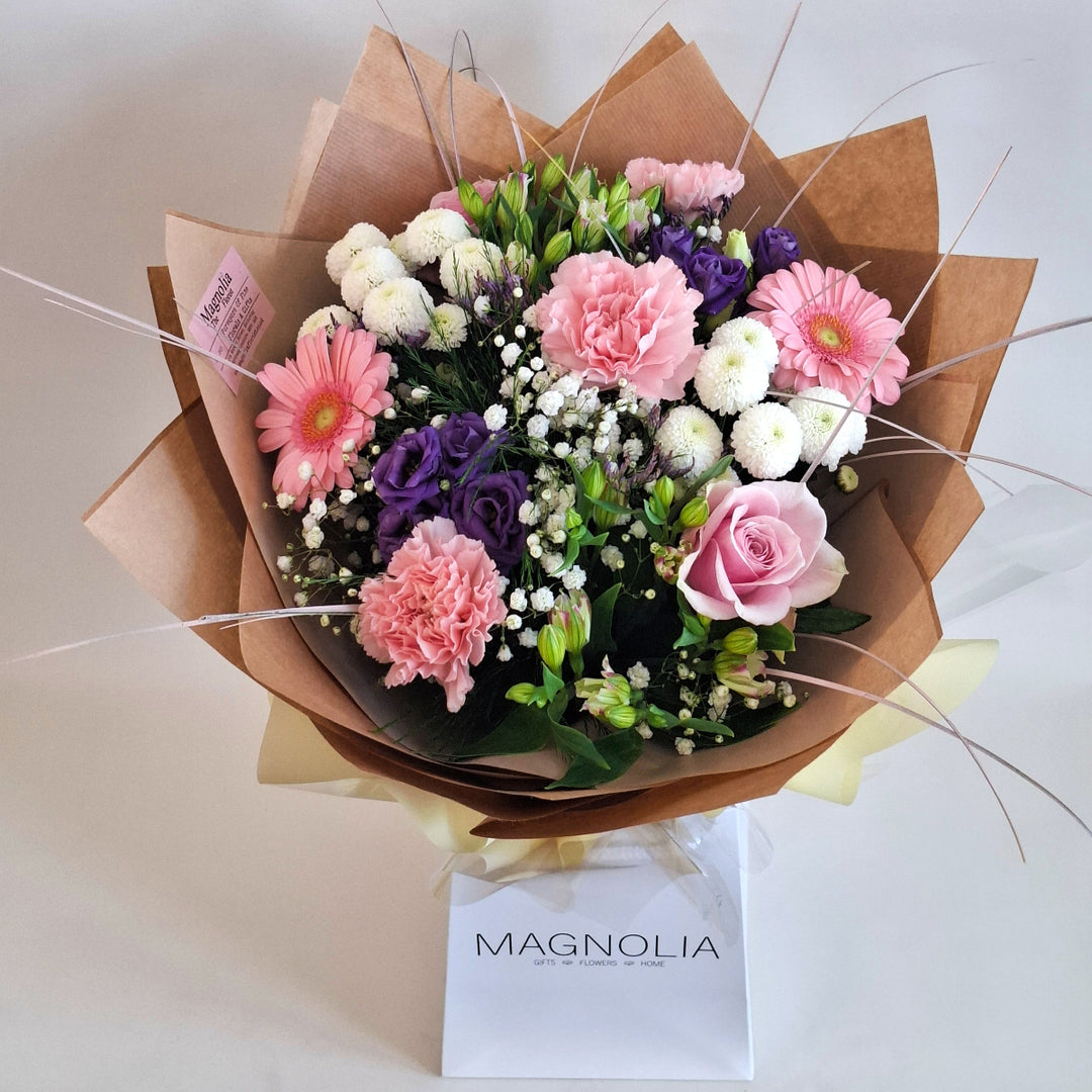 Bouquet of flowers wrapped in brown paper, in shade sof pink, white and purple and in a Magnolia the Florist Branded Bag.