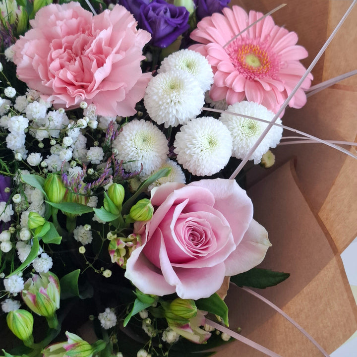 Bouquet of flowers wrapped in brown paper, in shade sof pink, white and purple and in a Magnolia the Florist Branded Bag.