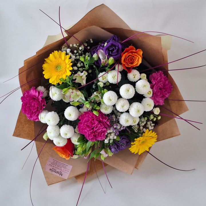 Bouquet of Vibrant flowers wrapped in brown paper, presented in a Magnolia the Florist branded bag.