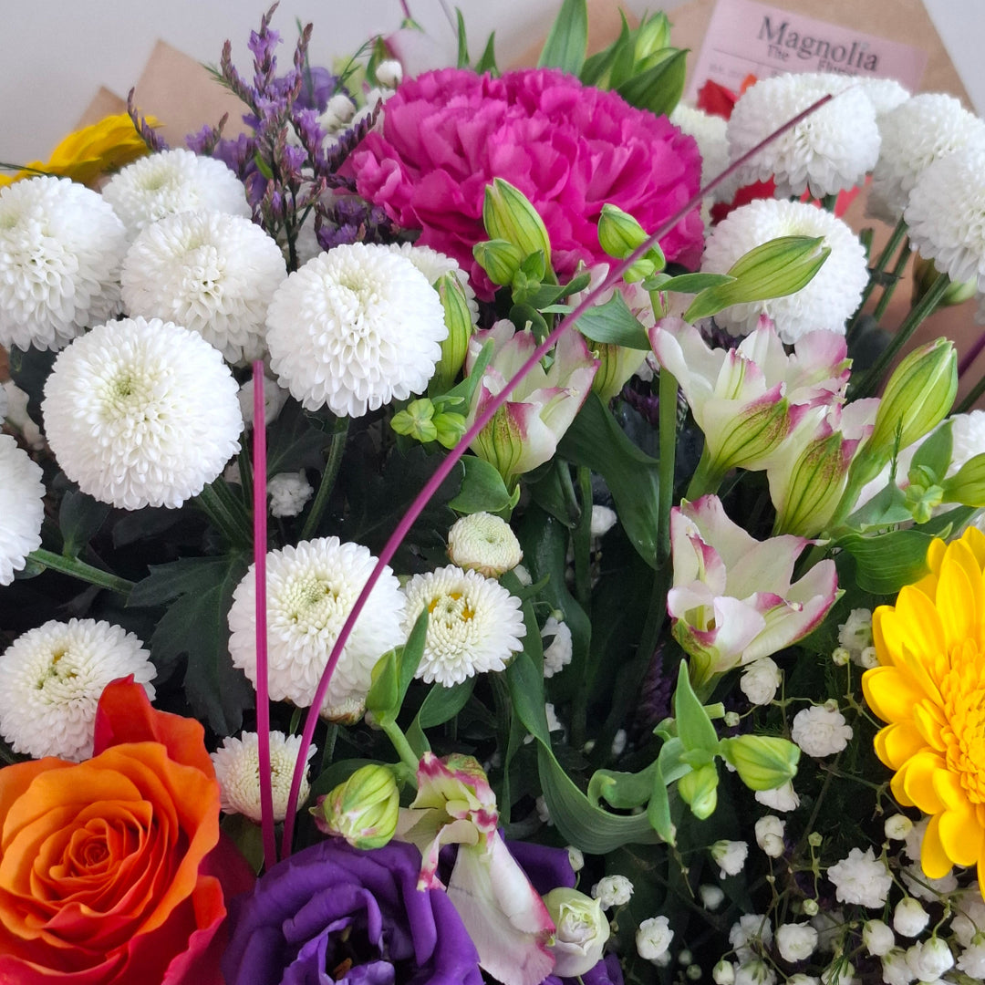 Bouquet of Vibrant flowers wrapped in brown paper, presented in a Magnolia the Florist branded bag.